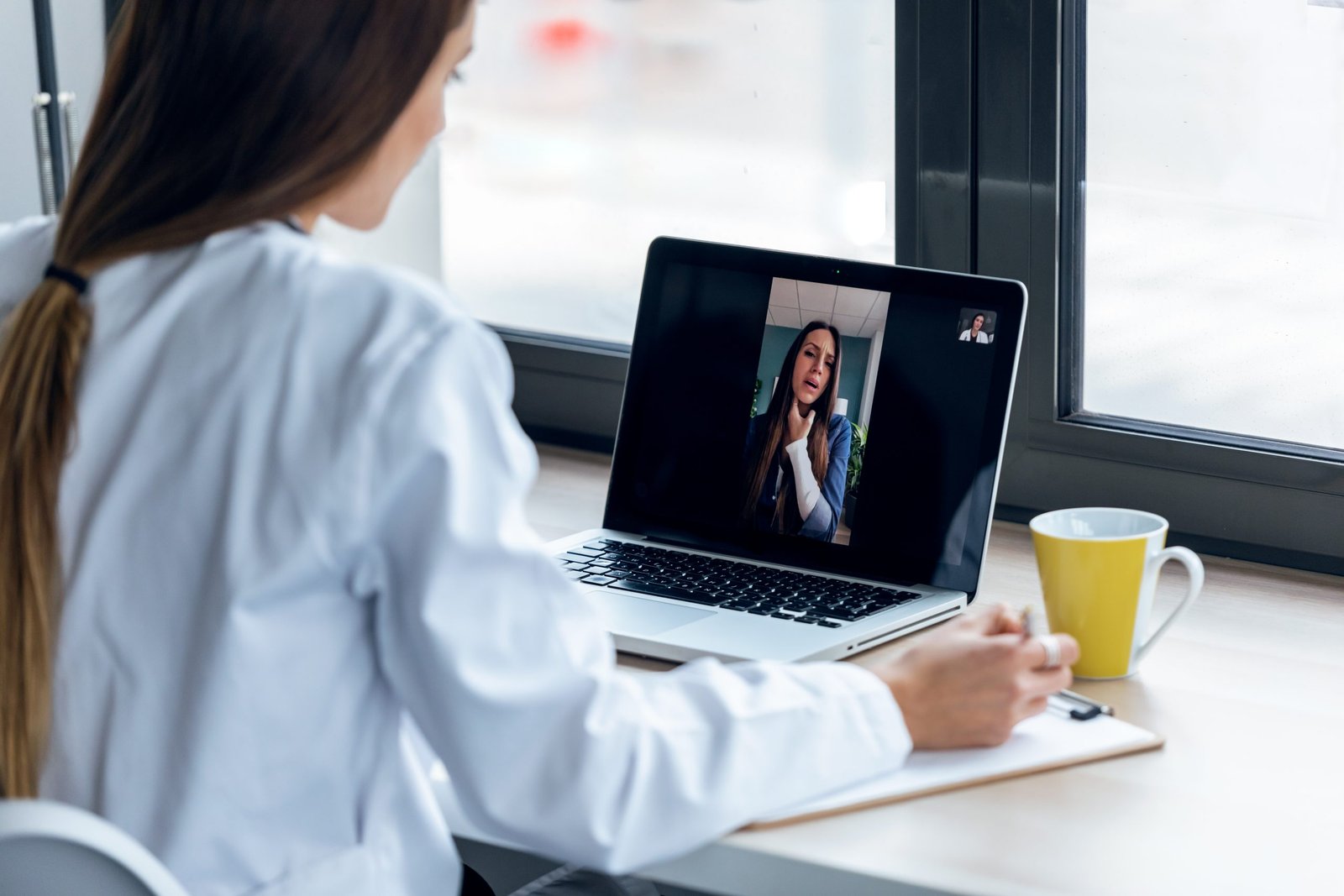 Shot of back view of a doctor attending to a woman patient through a video call with the laptop at home.